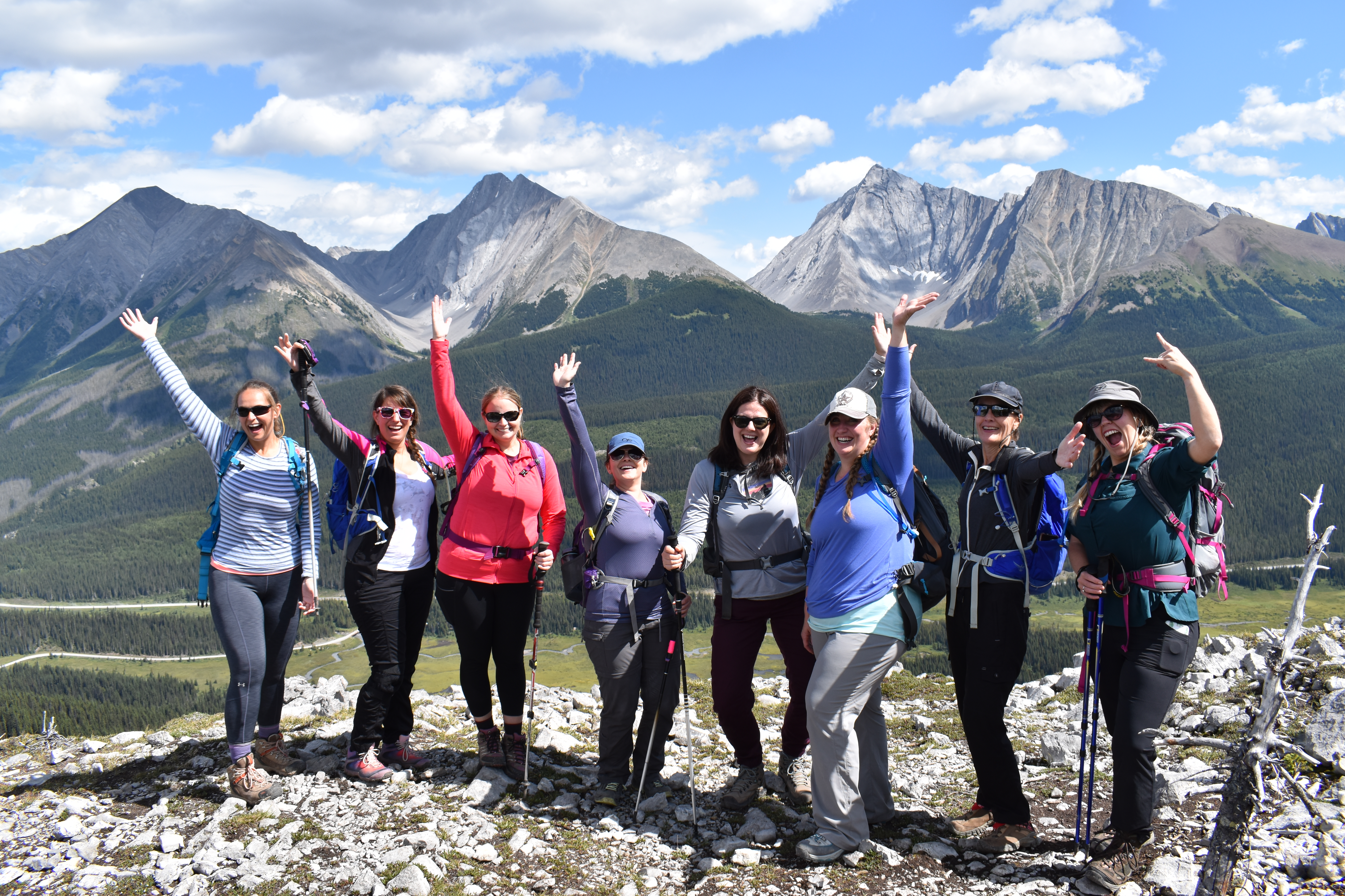A group of Explorer Chick women raise their arms and smile at the camera while hiking on a single women group travel tour