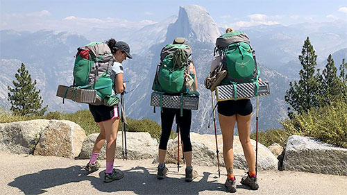 Three Explorer Chick women wearing backpacking packs overlooking Half Dome in Yosemite National Park