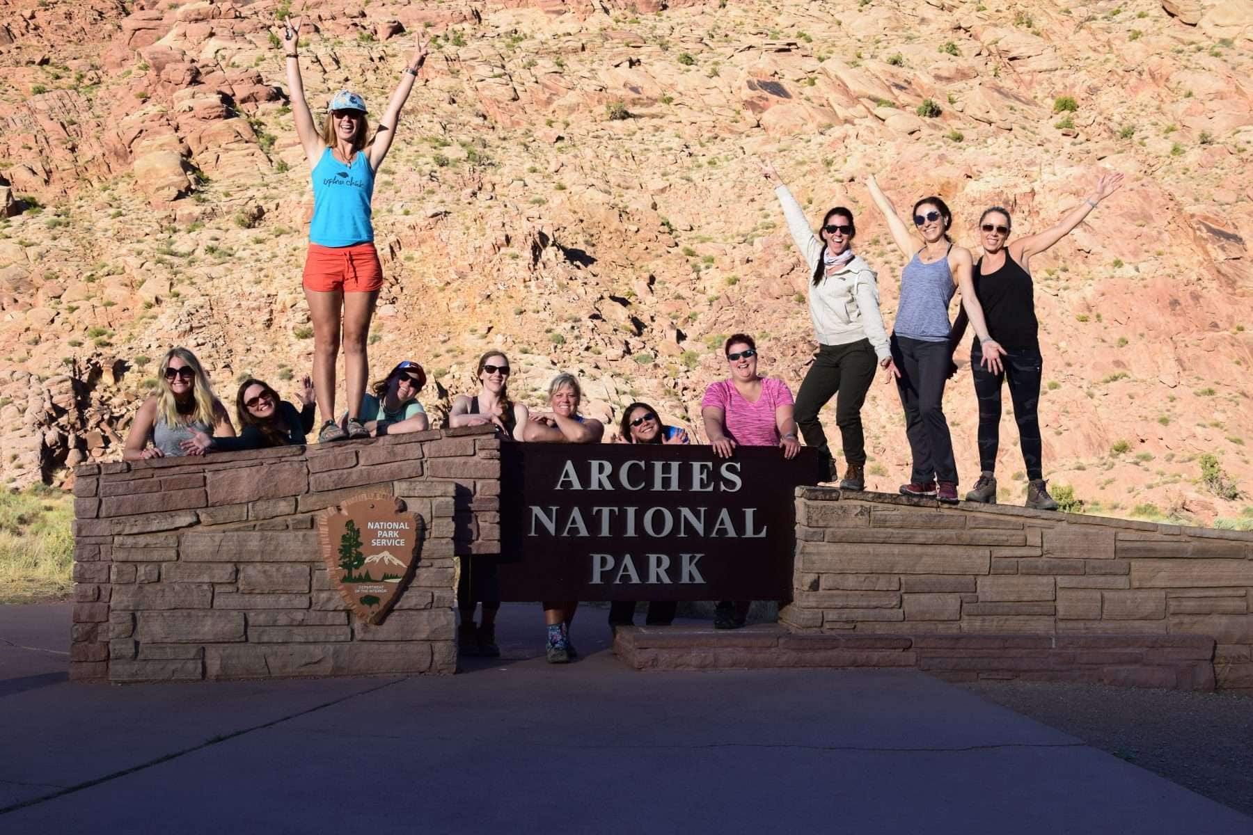 Women standing and posing on top of Arches National Park sign.