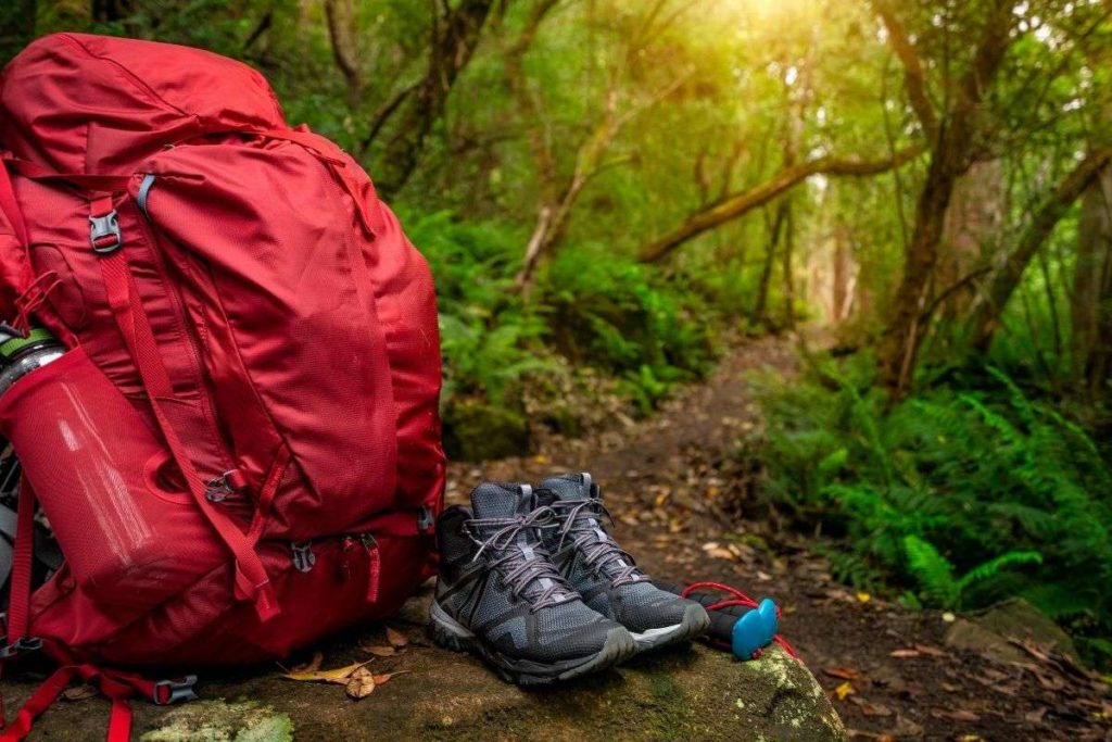 A pair of hiking boots sitting next to a red backpacking pack in the forest