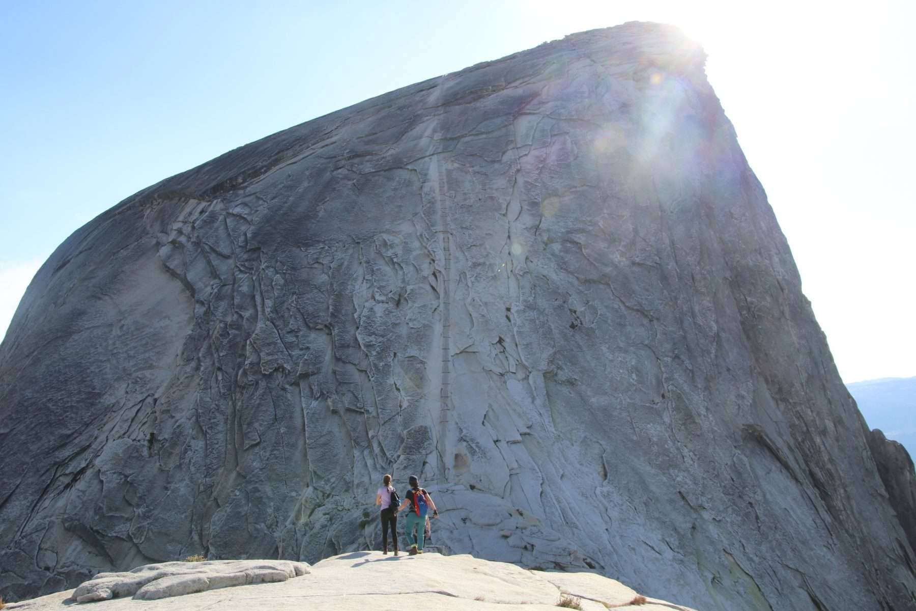 Two women wearing backpacks and standing in front of the Half Dome cables