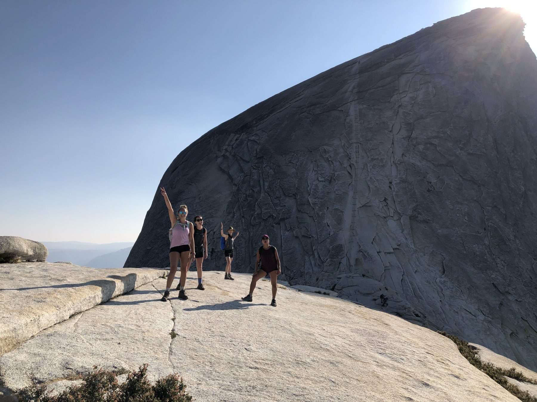 Women standing and posing with arms up during a hike in front of Half Dome as the sun is setting