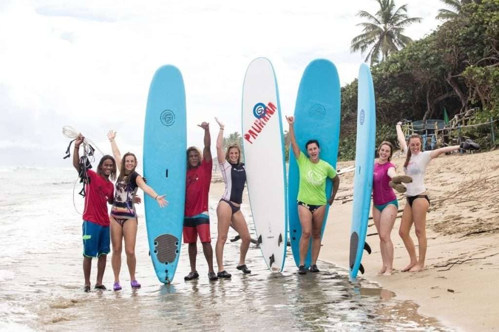 A small group of women on the beach carrying surfboards