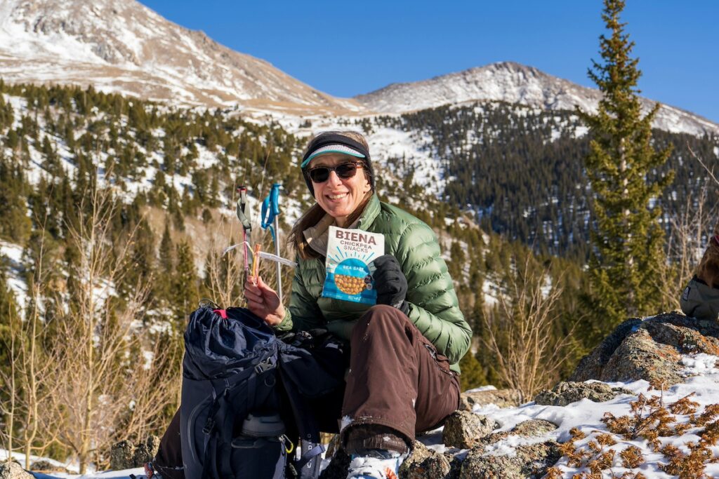 a woman holds up chickpeas hiking snacks while taking a break on trail