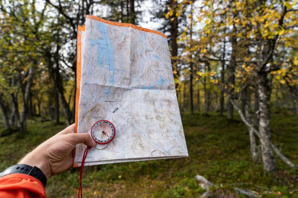 A POV shot of a hand holding up a paper map and compass in the woods