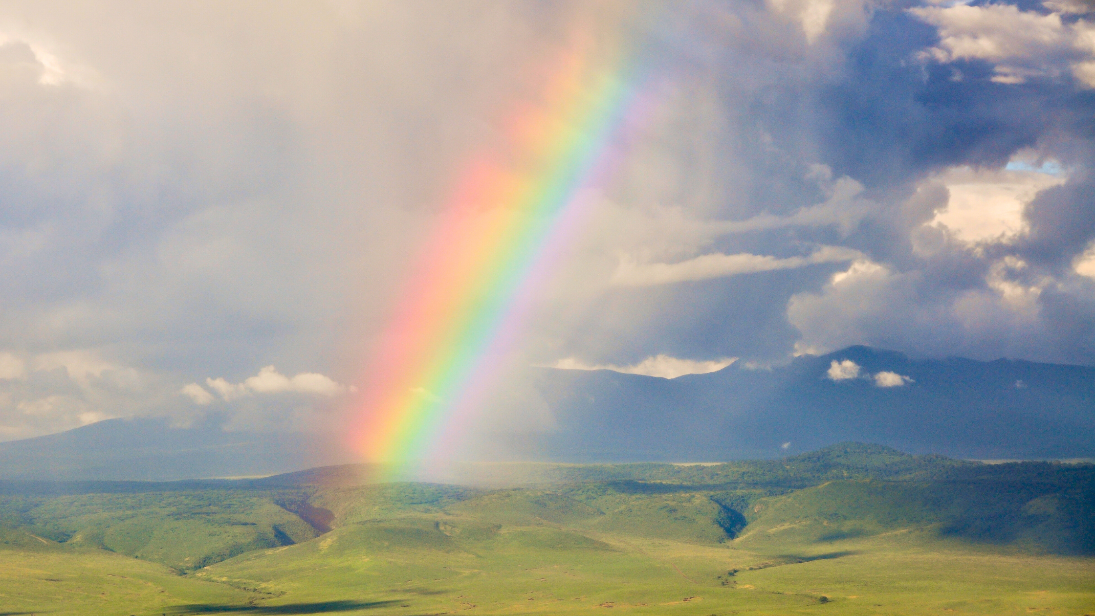 A vibrant rainbow stretching across the green highlands of Ngorongoro Crater in Tanzania.