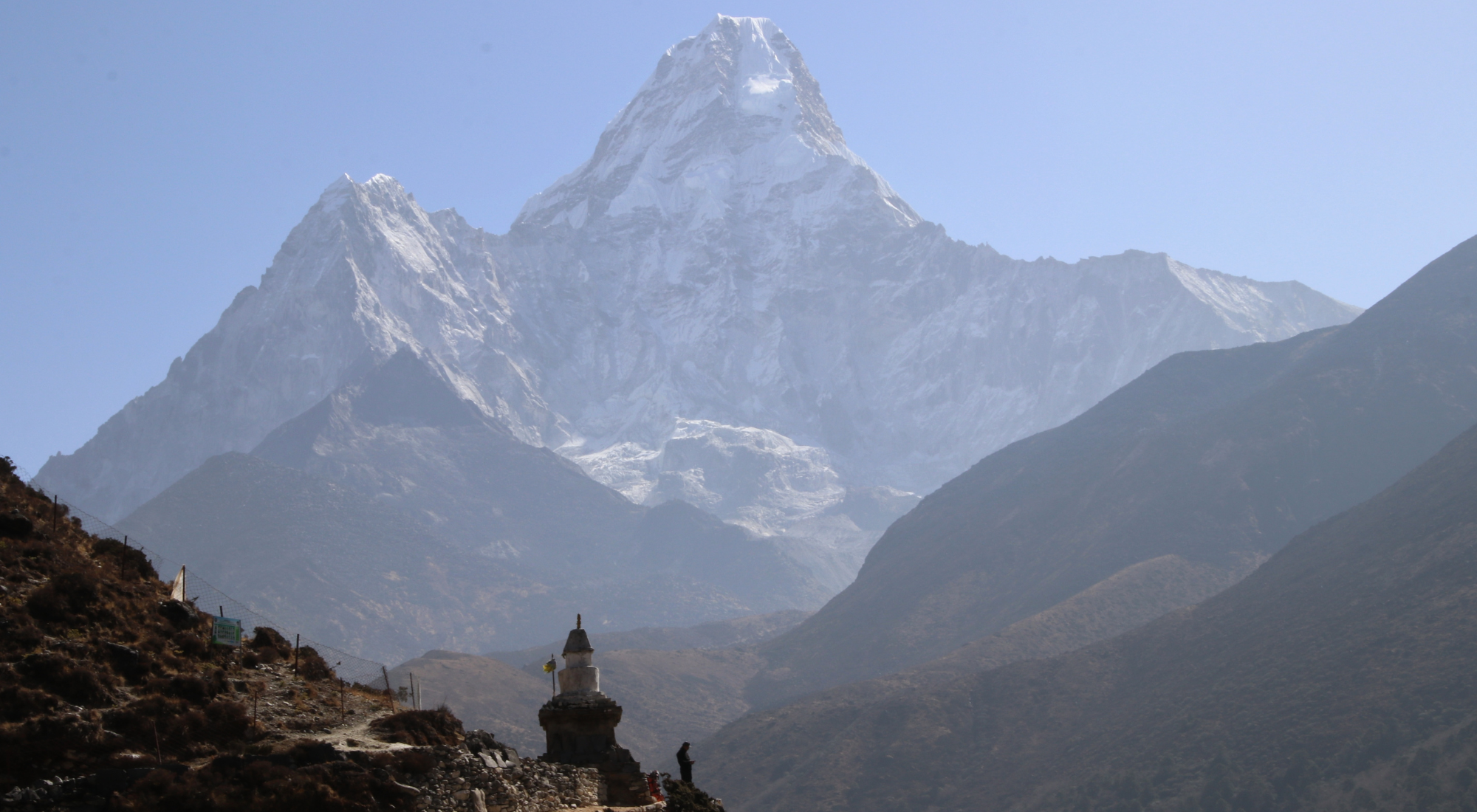 A white Buddhist stupa sits on a hillside with the dramatic snowcapped peak of Ama Dablam rising in the background on the Everest Base Camp trek.