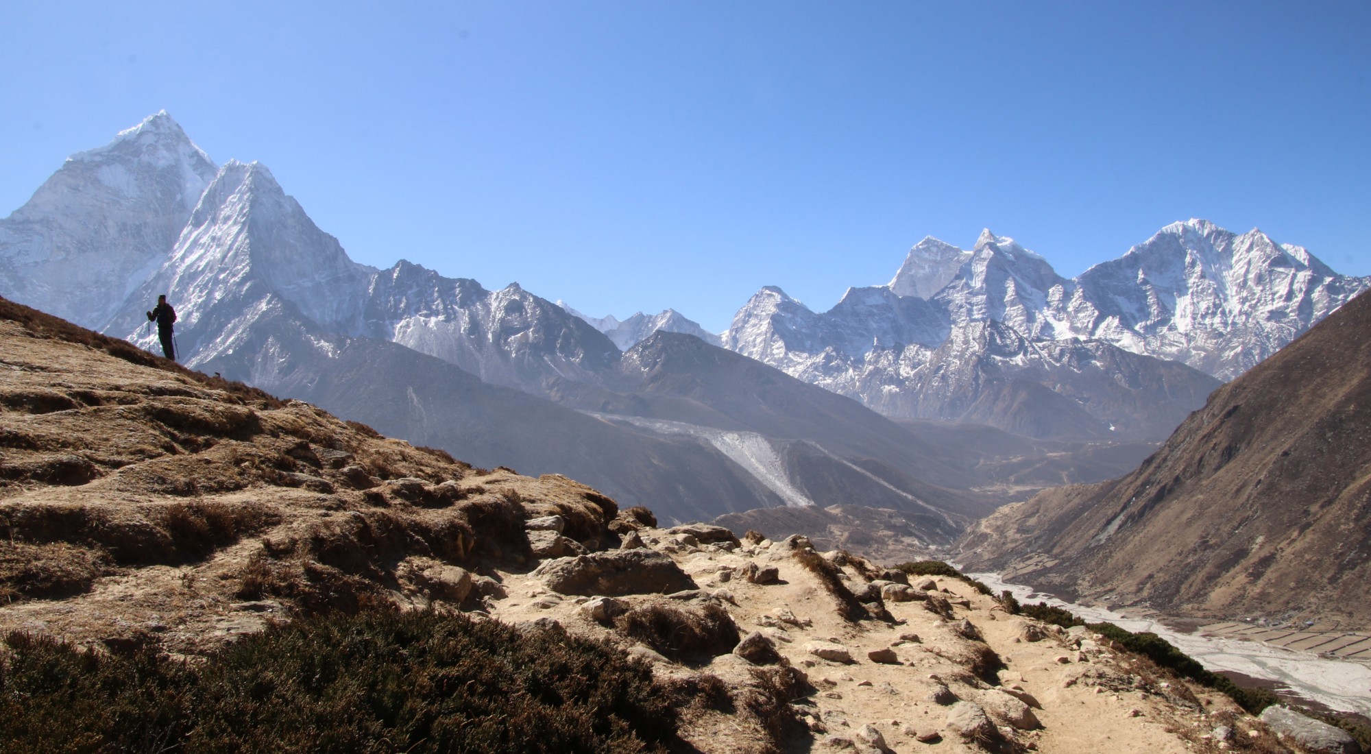 A solo hiker walks along a mountain ridge with sweeping views of Ama Dablam and surrounding Himalayan peaks on the way to Everest Base Camp.