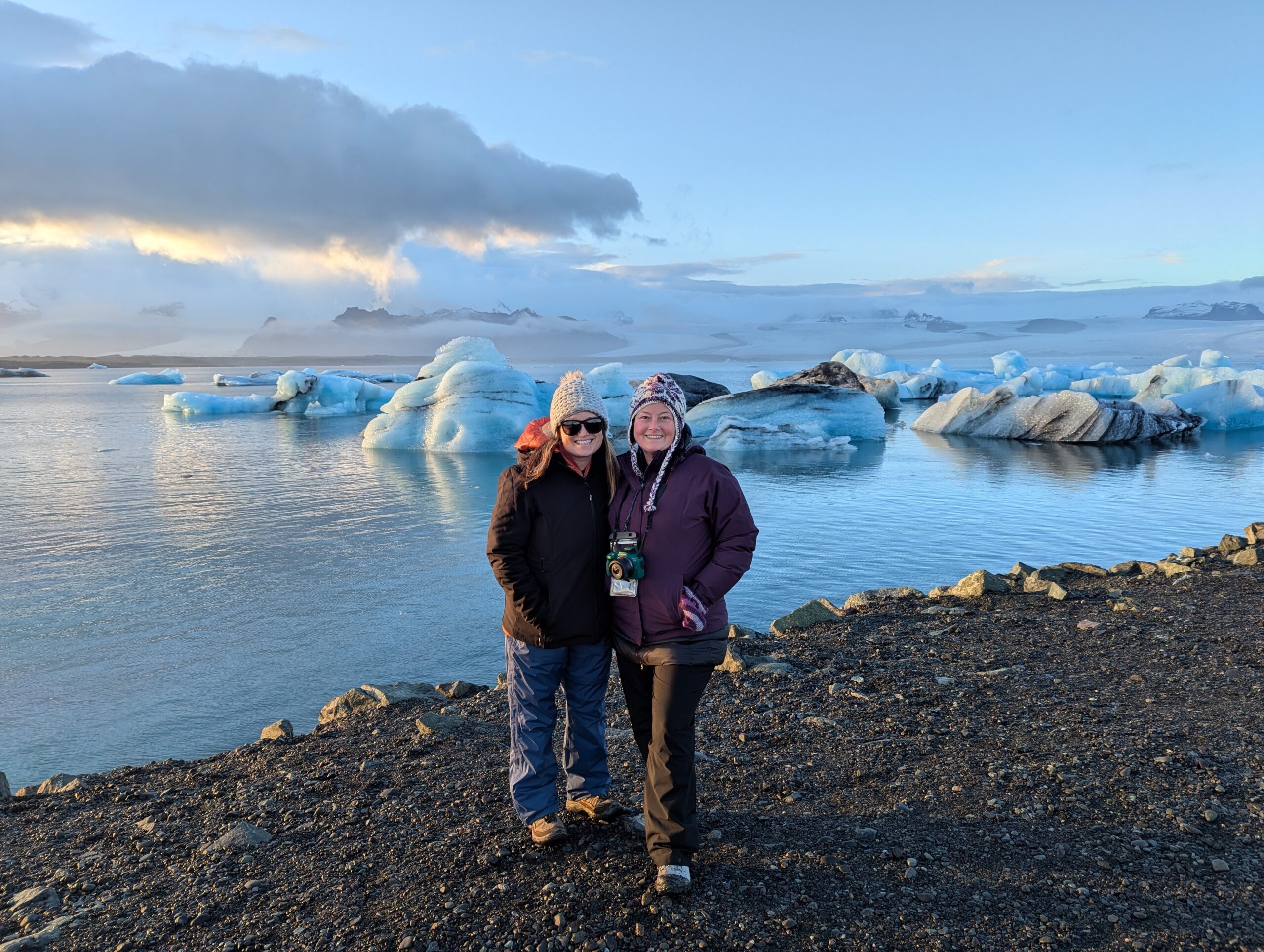 wo women smiling in front of a lagoon filled with blue icebergs in Iceland, capturing the spirit of Explorer Chick’s women-only adventures that blend breathtaking scenery, connection, and unforgettable moments.