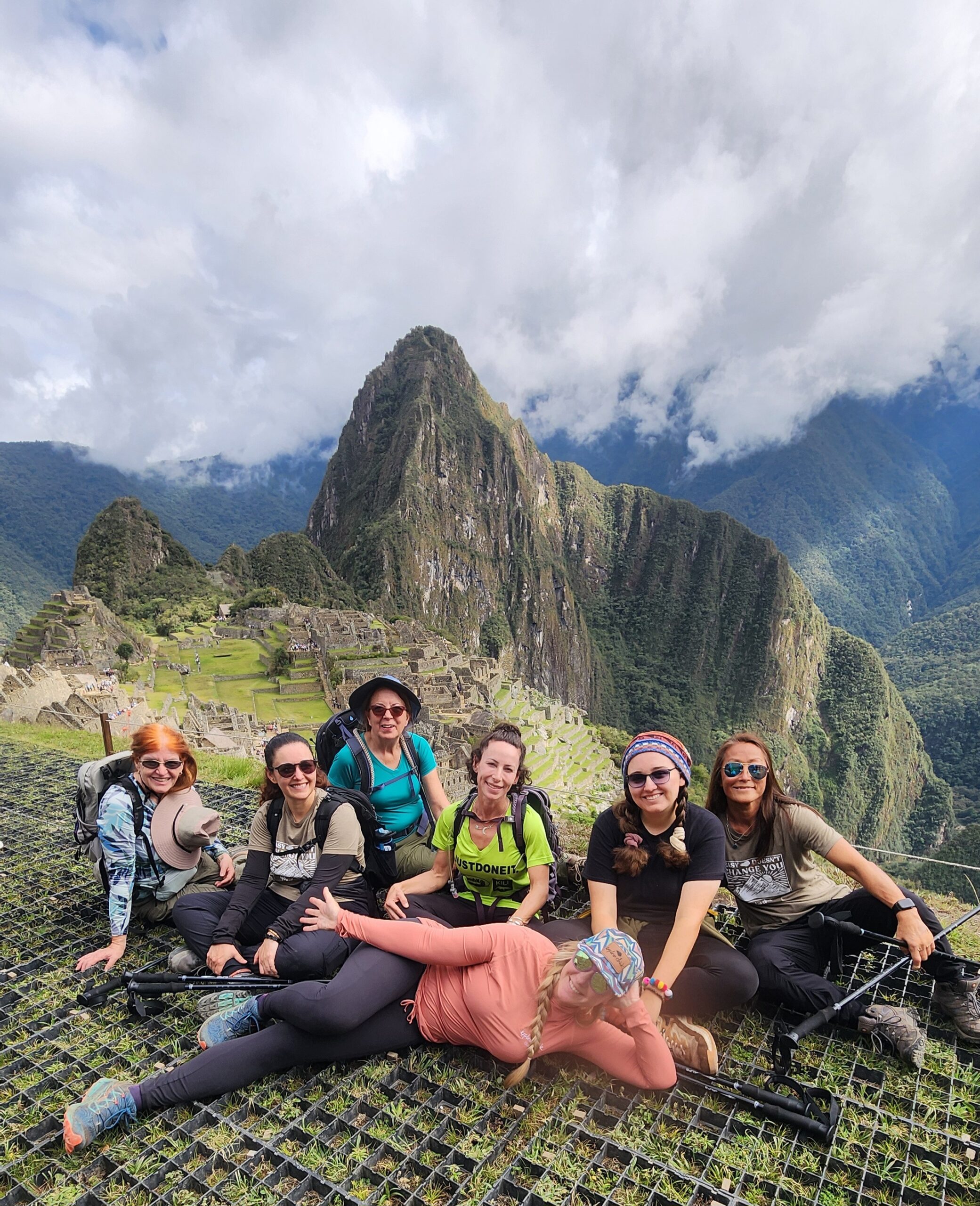 A group of women hikers posing with trekking poles at Machu Picchu, Peru, surrounded by lush green mountains during an Explorer Chick women-only adventure tour.