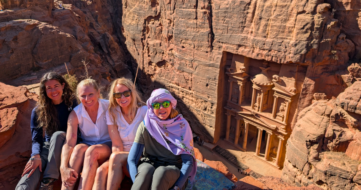 Group of women sitting on a cliff overlooking the Treasury at Petra in Jordan during a guided Explorer Chick adventure trip