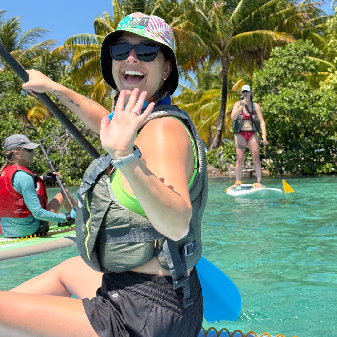 woman smiling and waving on a sup board in belize on a group trip.
