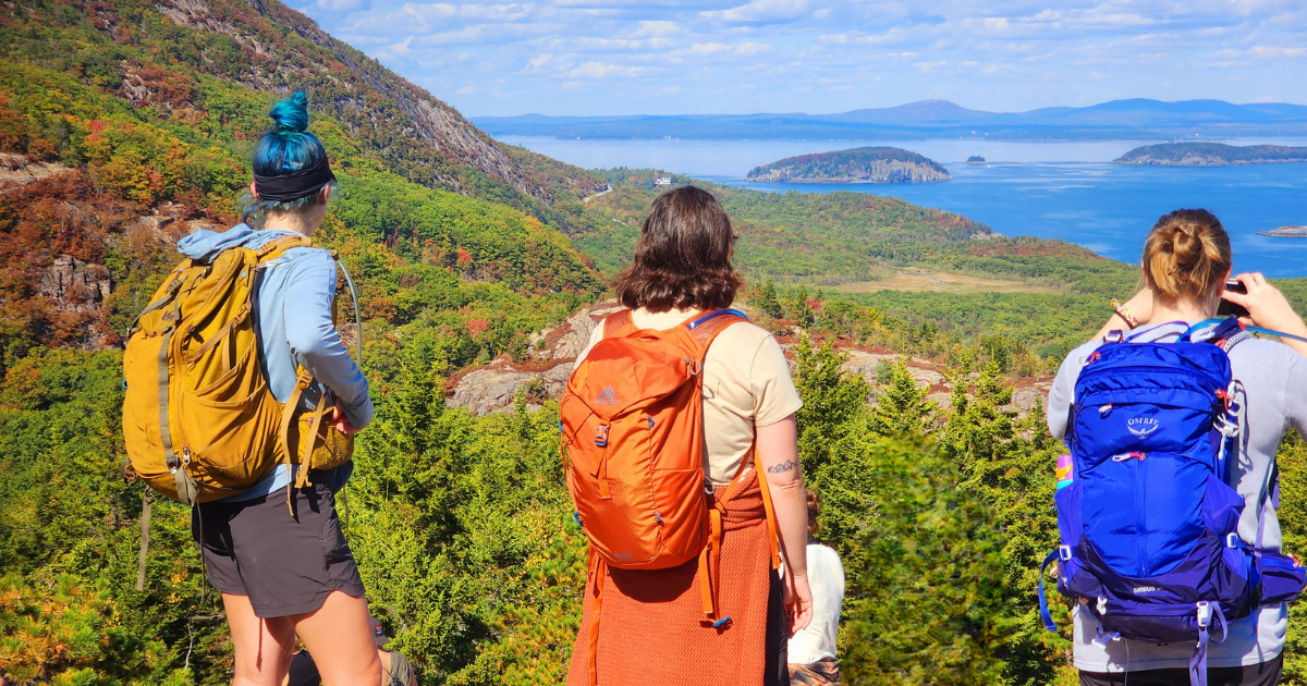 Women hiking in Acadia National Park with Explorer Chick overlooking coastal mountains and ocean views in Maine
