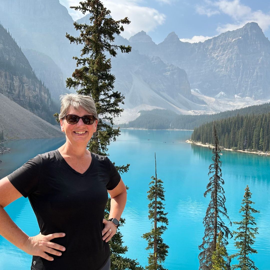 Woman at Moraine Lake in Banff National Park with turquoise water and dramatic mountain peaks in the background during an Explorer Chick adventure