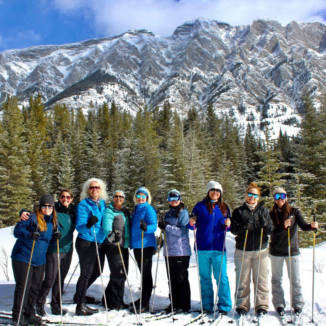 Group of women snowshoeing in Banff National Park with snow-covered mountains and pine forest in the background during an Explorer Chick winter adventure
