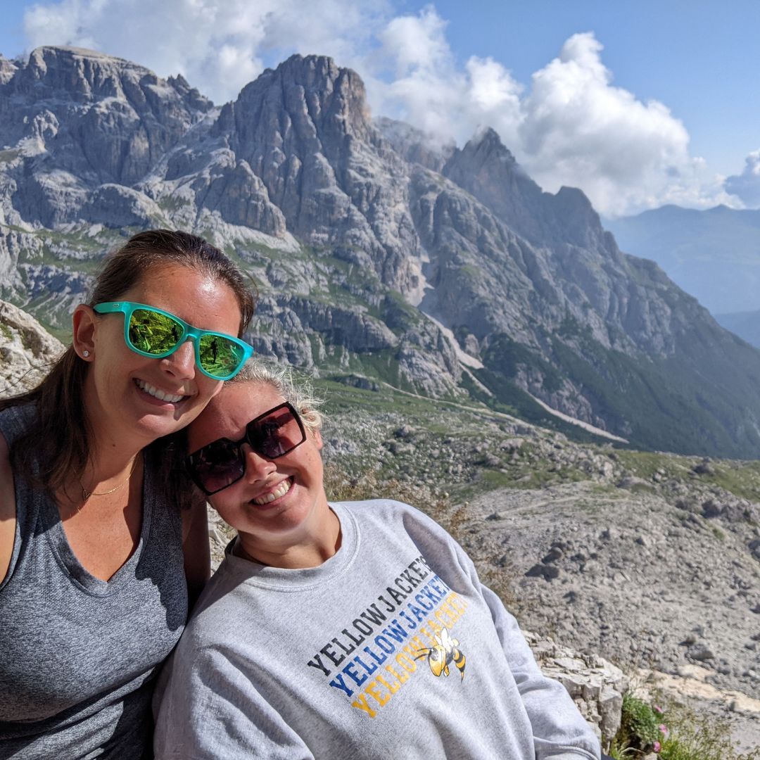 Two women hiking in the Italian Dolomites with dramatic rocky mountain peaks in the background during an Explorer Chick adventure