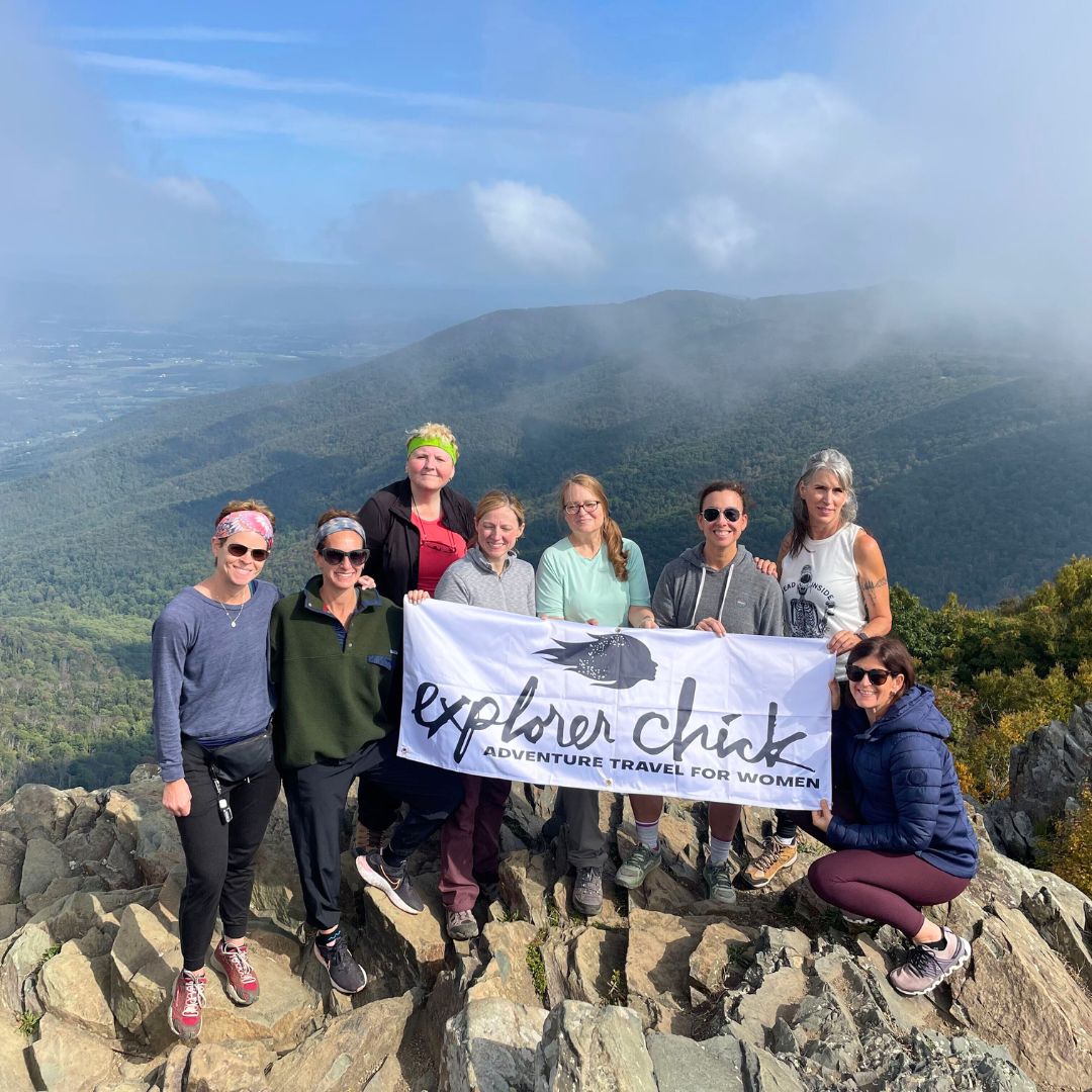 Explorer Chick women’s hiking group holding a banner at a mountain summit overlook in Shenandoah National Park during a scenic group adventure