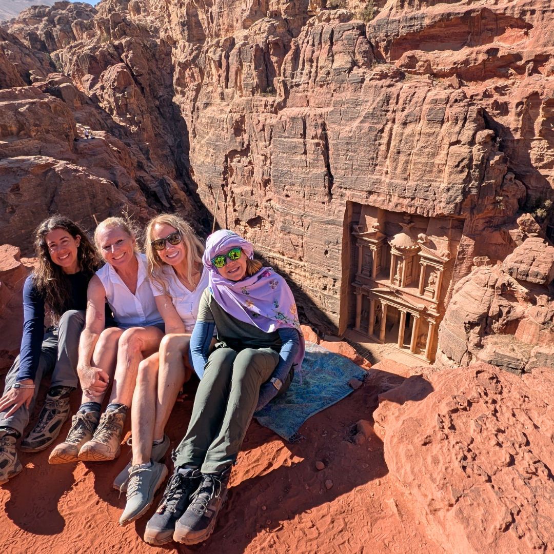 Four women overlooking the Monastery in Petra, Jordan during an Explorer Chick adventure with the iconic ancient rock-carved facade below