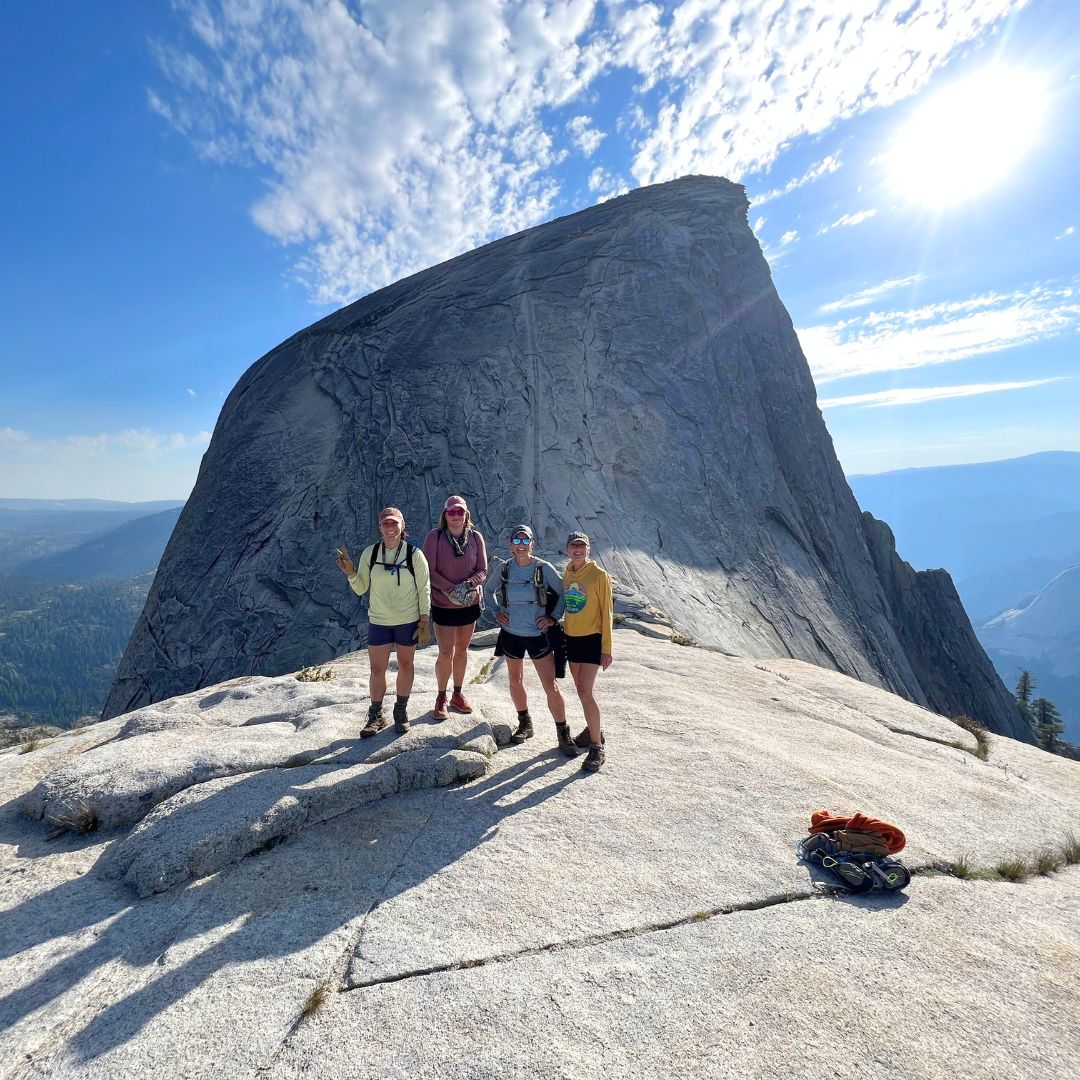 Four women hikers standing on Half Dome in Yosemite National Park with dramatic granite views during an Explorer Chick adventure