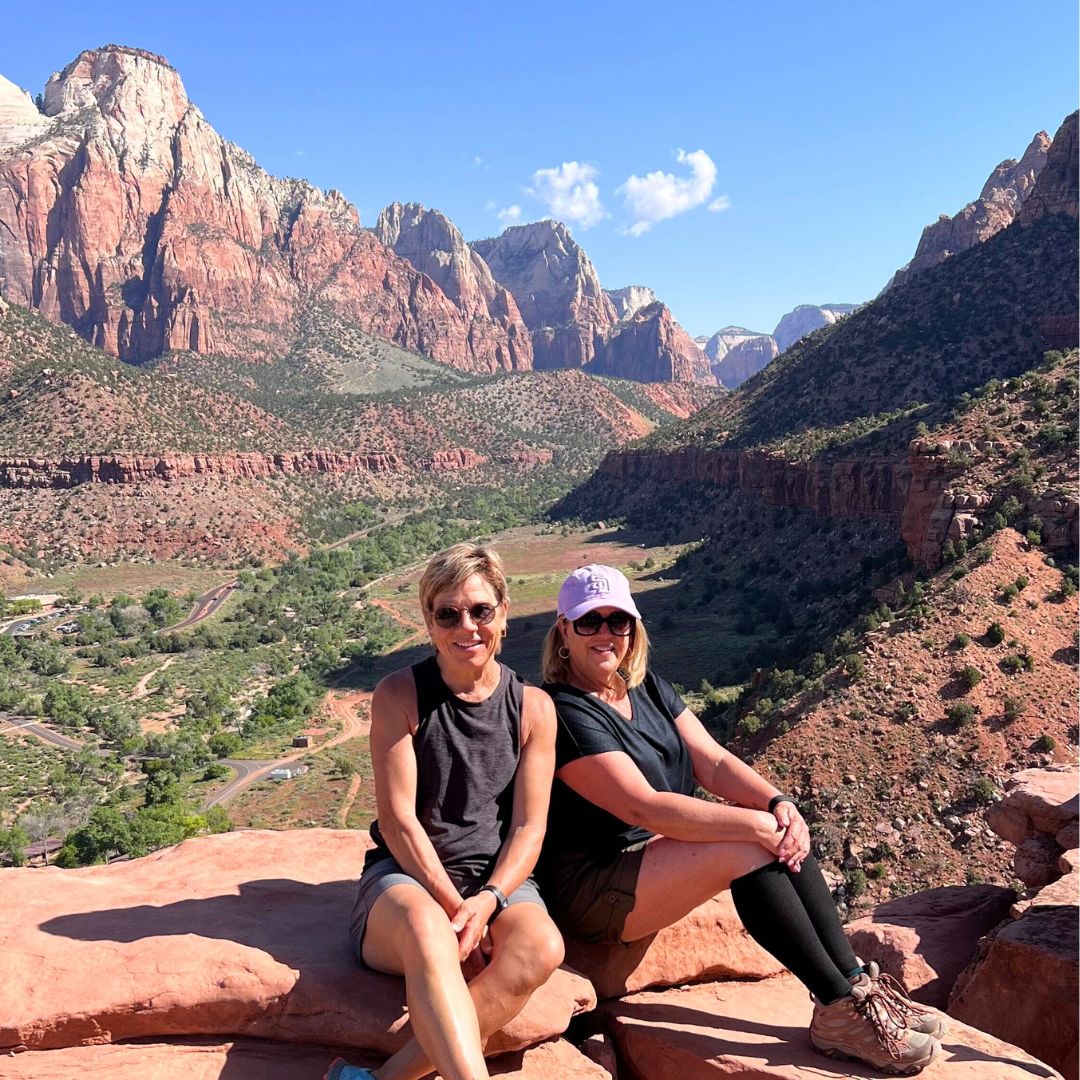 Two women at a scenic overlook in Zion National Park with red rock cliffs and canyon views in the background during an Explorer Chick adventure
